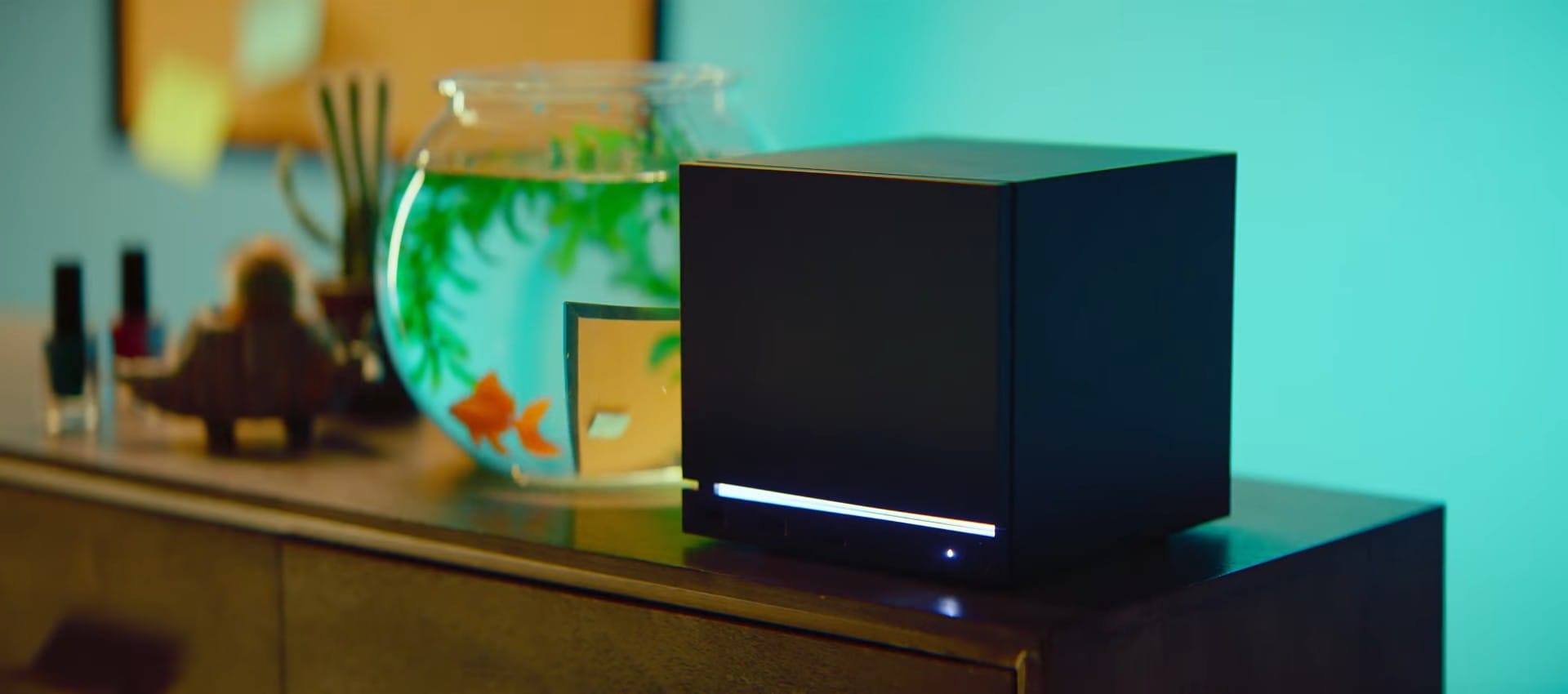 A Steam Machine, which is a small cuboid computer, on a TV unit next to a fish bowl.