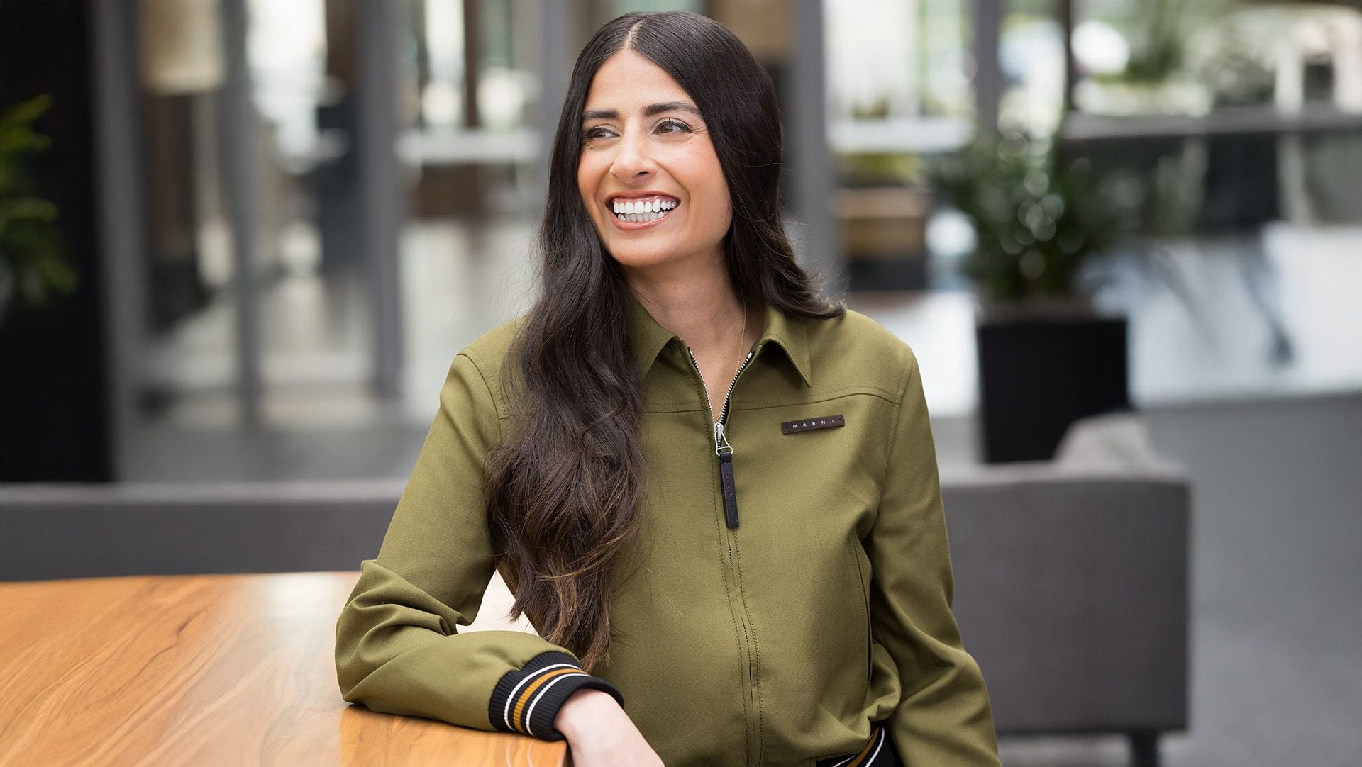 Asha Sharma, the head of Xbox, smiles and leans on a elbow-high desk.