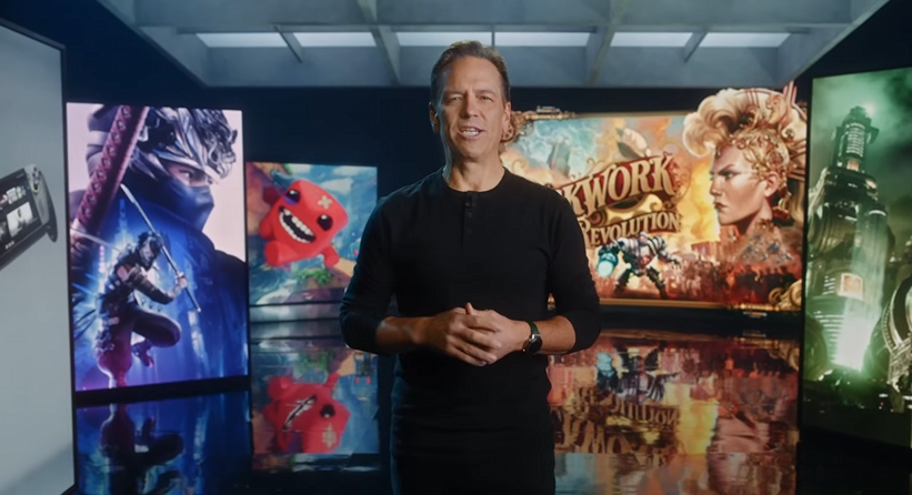 Phil Spencer standing in front of large screens showing game artwork in an Xbox showcase.