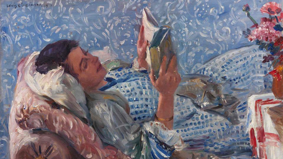 A woman reclines on a chaise longue, reading a book. She's wearing blue and is backgrounded by a blue wallpaper.
