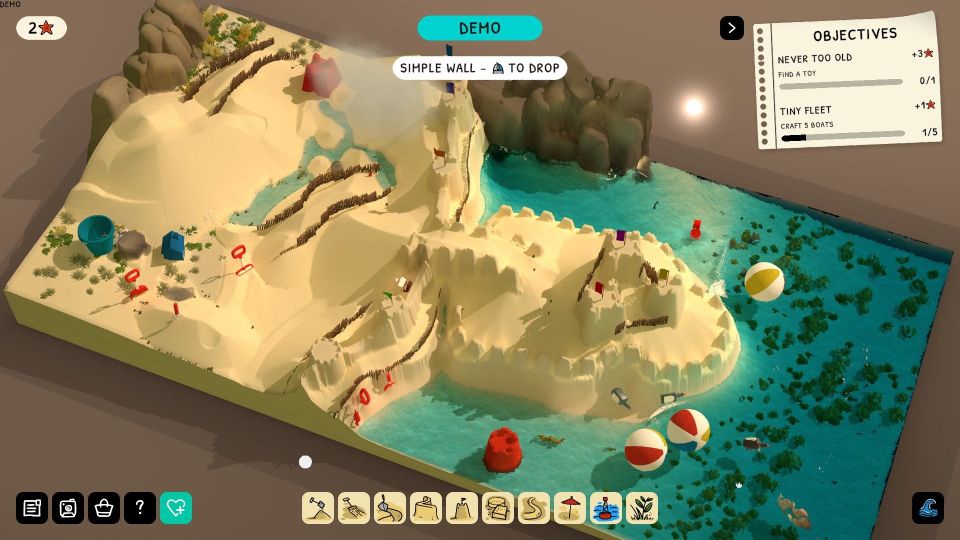 A sandcastle with crenellated walls on beach with some rocks nearby and beach balls floating in the tide.