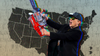 In a composite image, an absurdly ecstatic Elon Musk wields a chainsaw in front of a map of the United States.