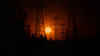 The sun sets behind high-tension power lines.