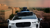 In a composite image, a Waymo car is seen over a view of Washington D.C. with the Washington Monument at center.