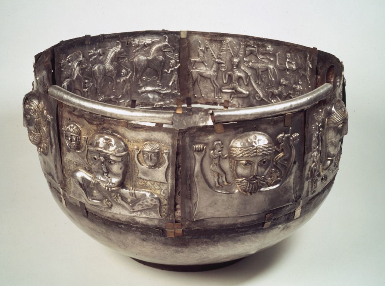 "El Caldero de Gundestrup, una antigua pieza de plata celta, con elaborados grabados y relieves que muestran figuras mitológicas y escenas rituales, incluyendo una posible representación de Cernunnos, el Dios de los Cuernos. Este artefacto histórico, datado entre los siglos I y II a.C., es un destacado ejemplo de la artesanía y las creencias religiosas de la cultura celta