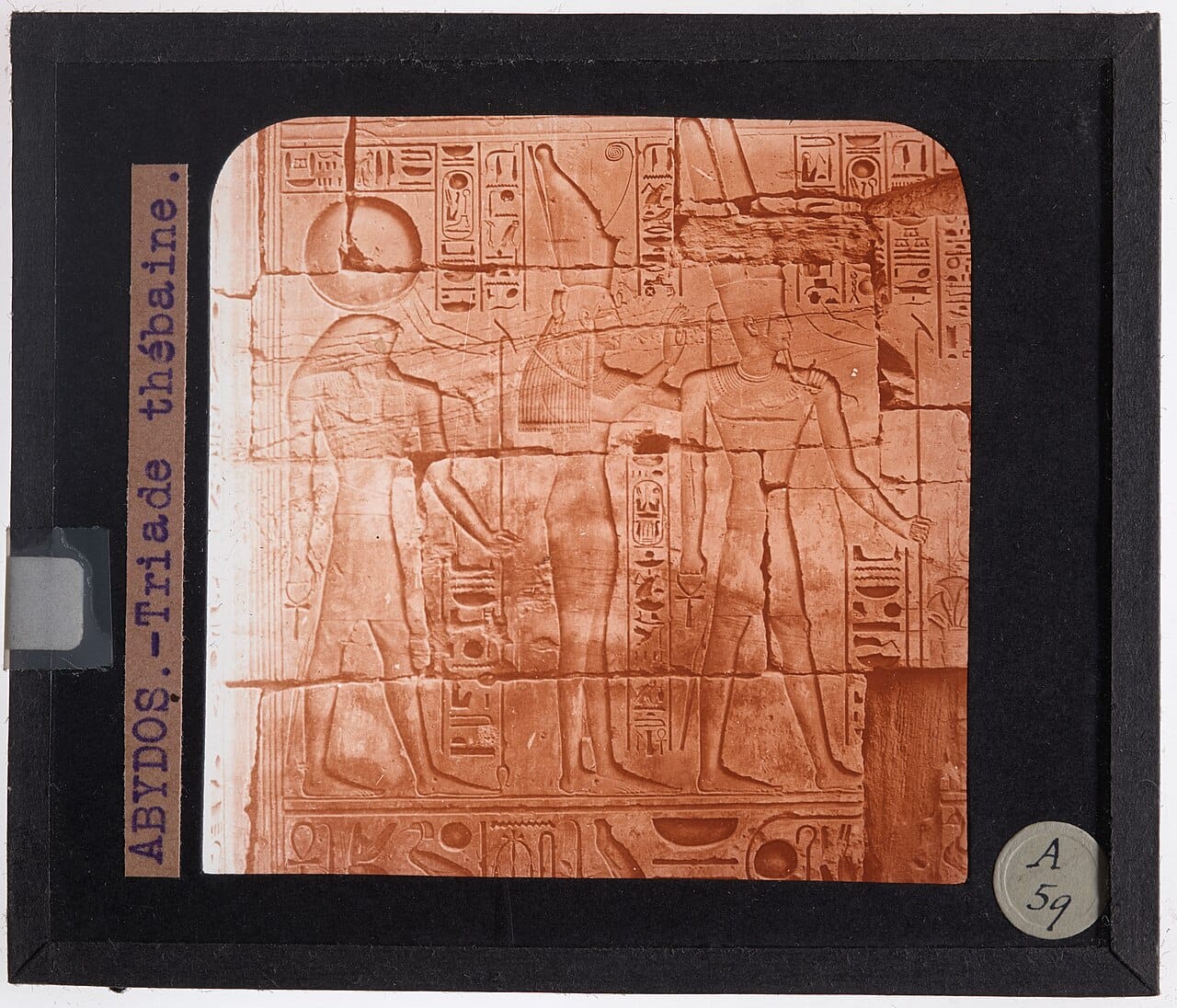 Relieve tallado en piedra de un templo egipcio mostrando a tres figuras de perfil: Horus con cabeza de halcón, Isis con un tocado de trono, y Osiris momificado sosteniendo el cayado y el mayal