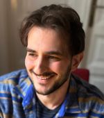 Profile picture of Mario, a young white man with dark hair and dark beard, smiling curiously. He's wearing a blue-striped pullover.