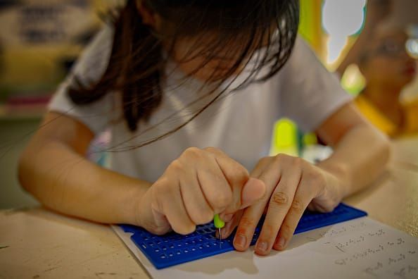 Photograph of a young Philippine girl using a braille slate and stylus to write on paper. She looks down, concentrated, her face covered by long dark hair.