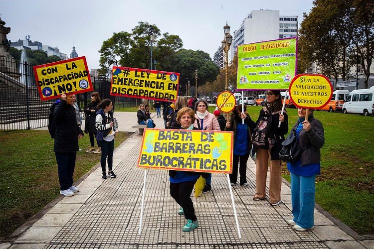 Photograph of a group of protestors holding yellow signs on a sidewalk.
