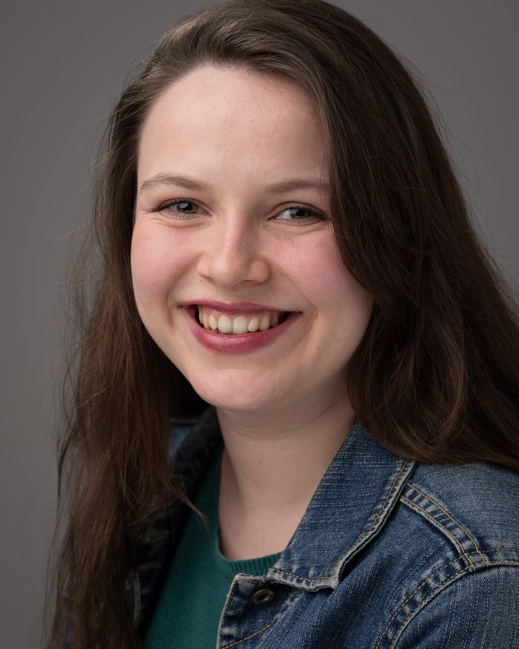 Profile picture of Blossom, a white woman in her twenties, with an open smile and long dark hair. She has engaging eyes, and wears a denim jacket.