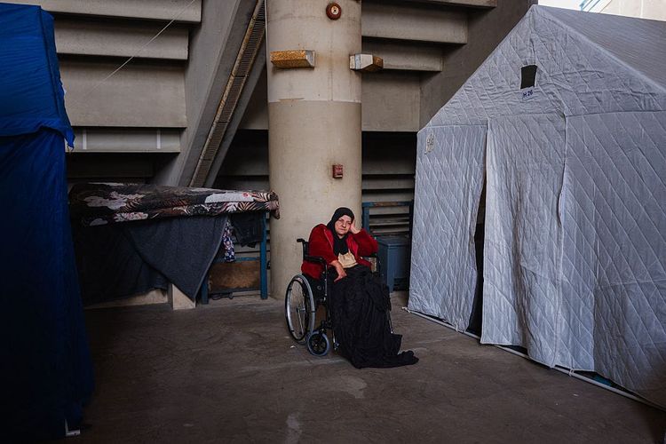 A photo of an older hijabi woman in a wheelchair next to a large white tent.