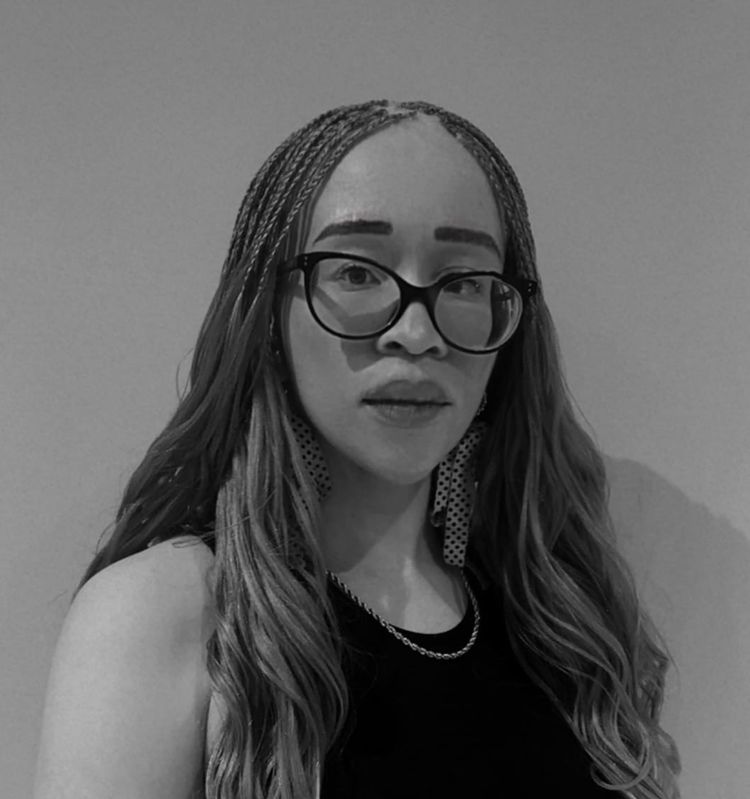 A black and white profile picture of Athenkosi, a young woman with albinism. She has braided long hair, big glasses and earrings and looks intently at the camera.
