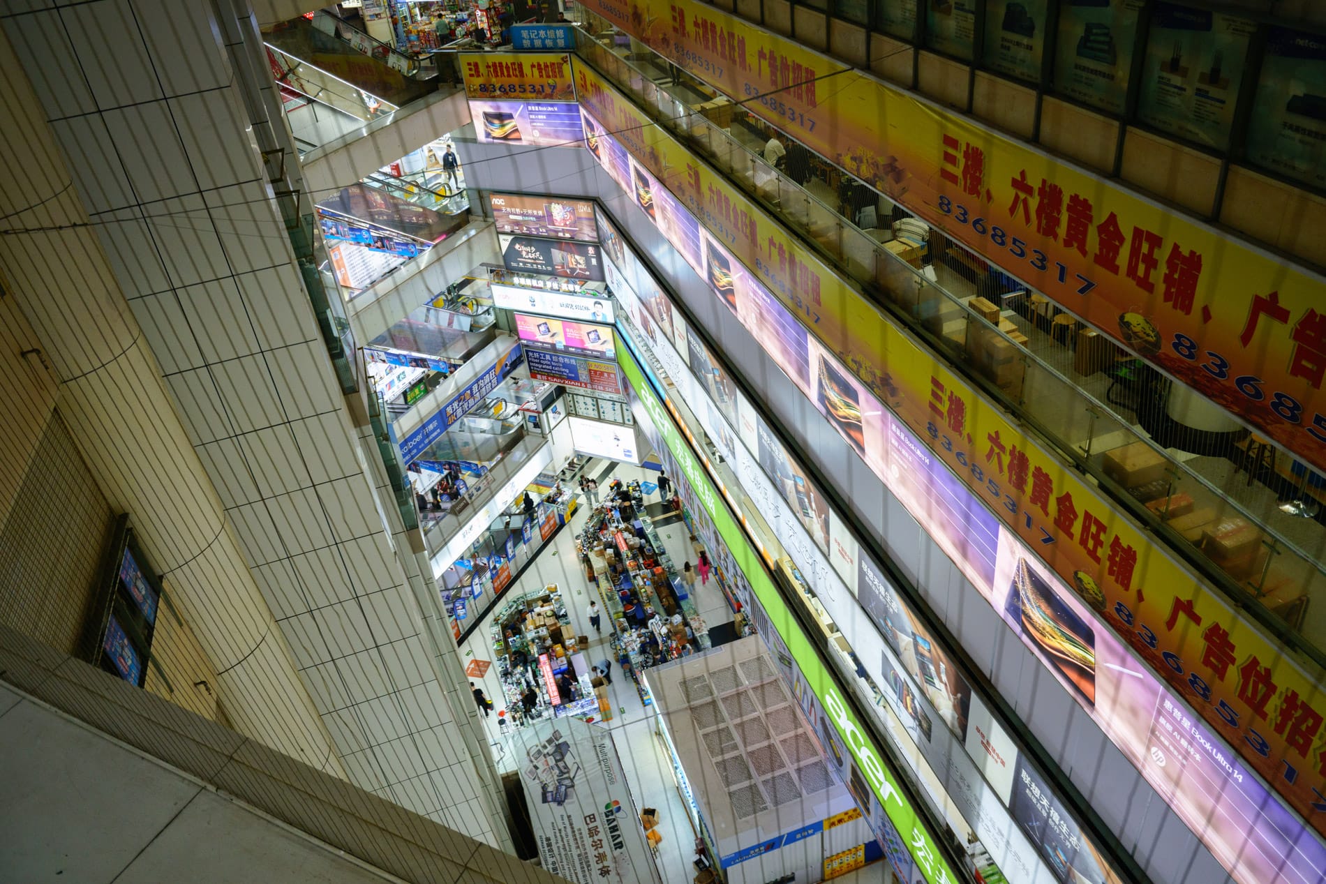 View from escalator of multiple floors of electronics market, backlit signage, distorted octagonal layout.
