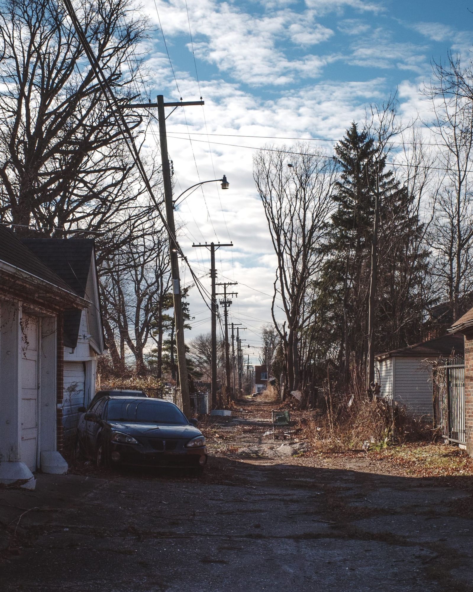 Dry winter alley with cracked pavement, power lines, old car and empty shopping cart.