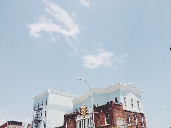 Apartment building siding painted light blue and white, matching above clouds and sky.