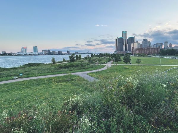 View from a hill near the Detroit river. Wetland plants, snaking concrete path, skyline and Windsor in the distance.