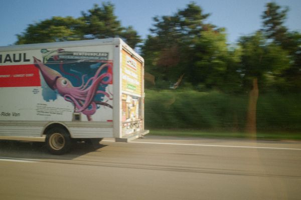 Rear end of U-Haul truck with squid graphics, shot from moving car, blurry trees whizzing by.