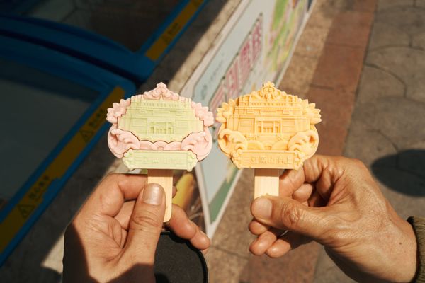 Two hands holding popsicles shaped like Buddhist temples, one pink and green, the other orange.