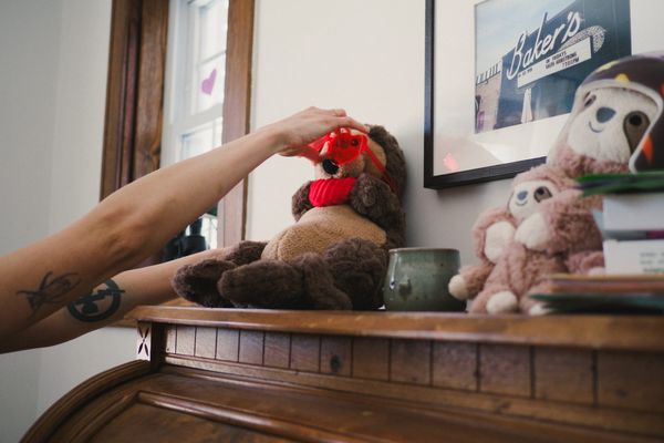 Arm placing heart-shaped red glasses over stuffed otter toy on roll-top desk