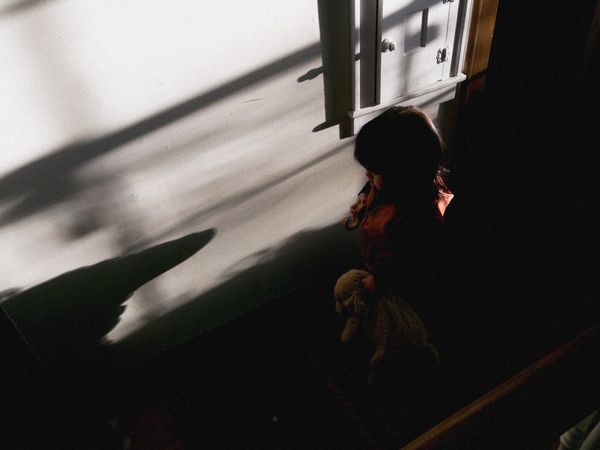 Rufus holding stuffed animal, near-dusk light with long, high contrast shadows from behind, plaster walls and wood door frame.
