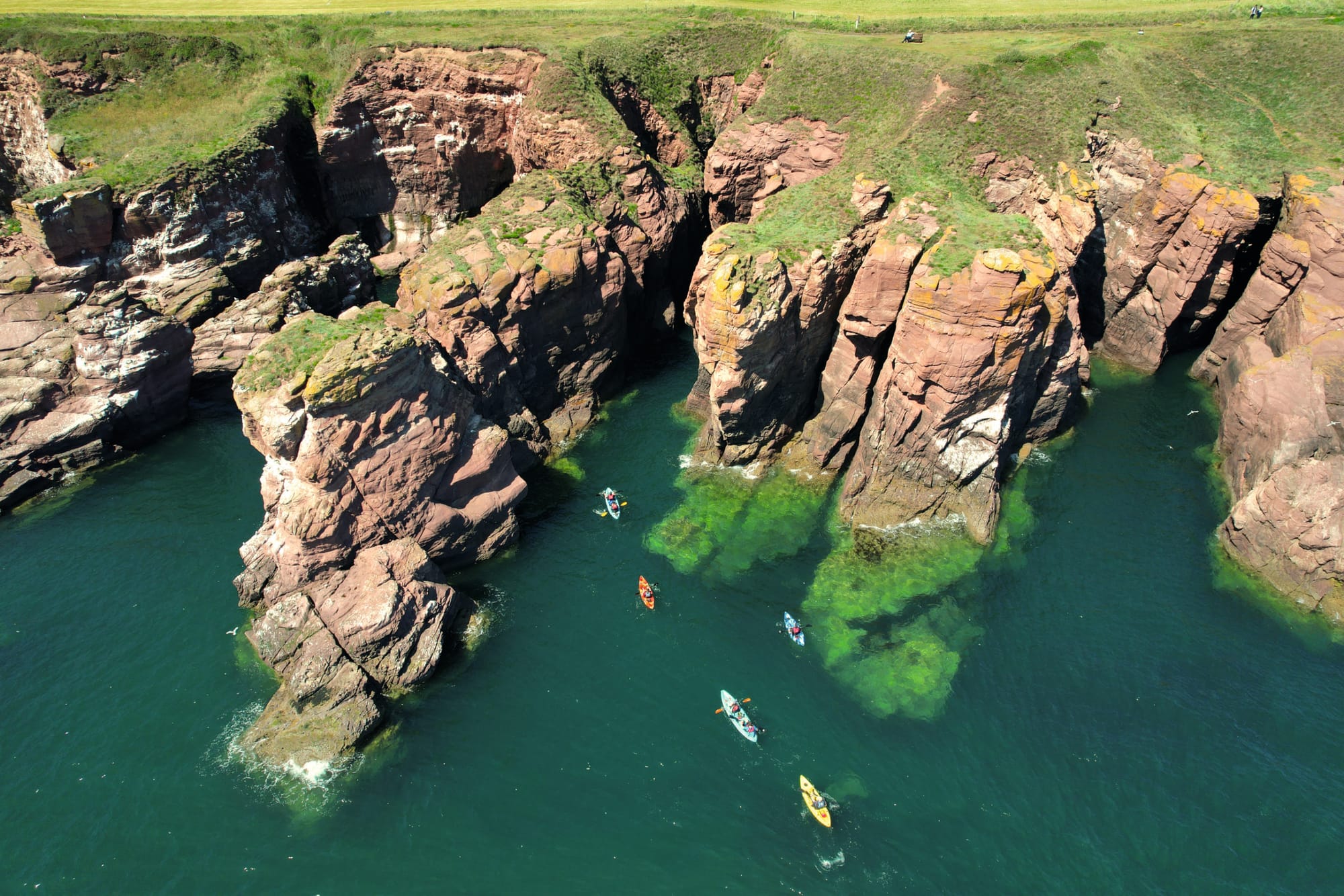 Aerial view of the red cliffs with kayaks going towards them.