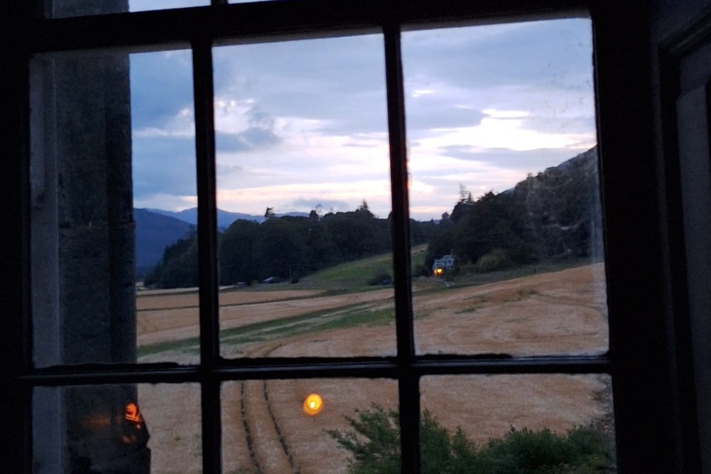 Looking out the castle's window across fields and to distant trees and hills. Candles are reflected in the window panes.