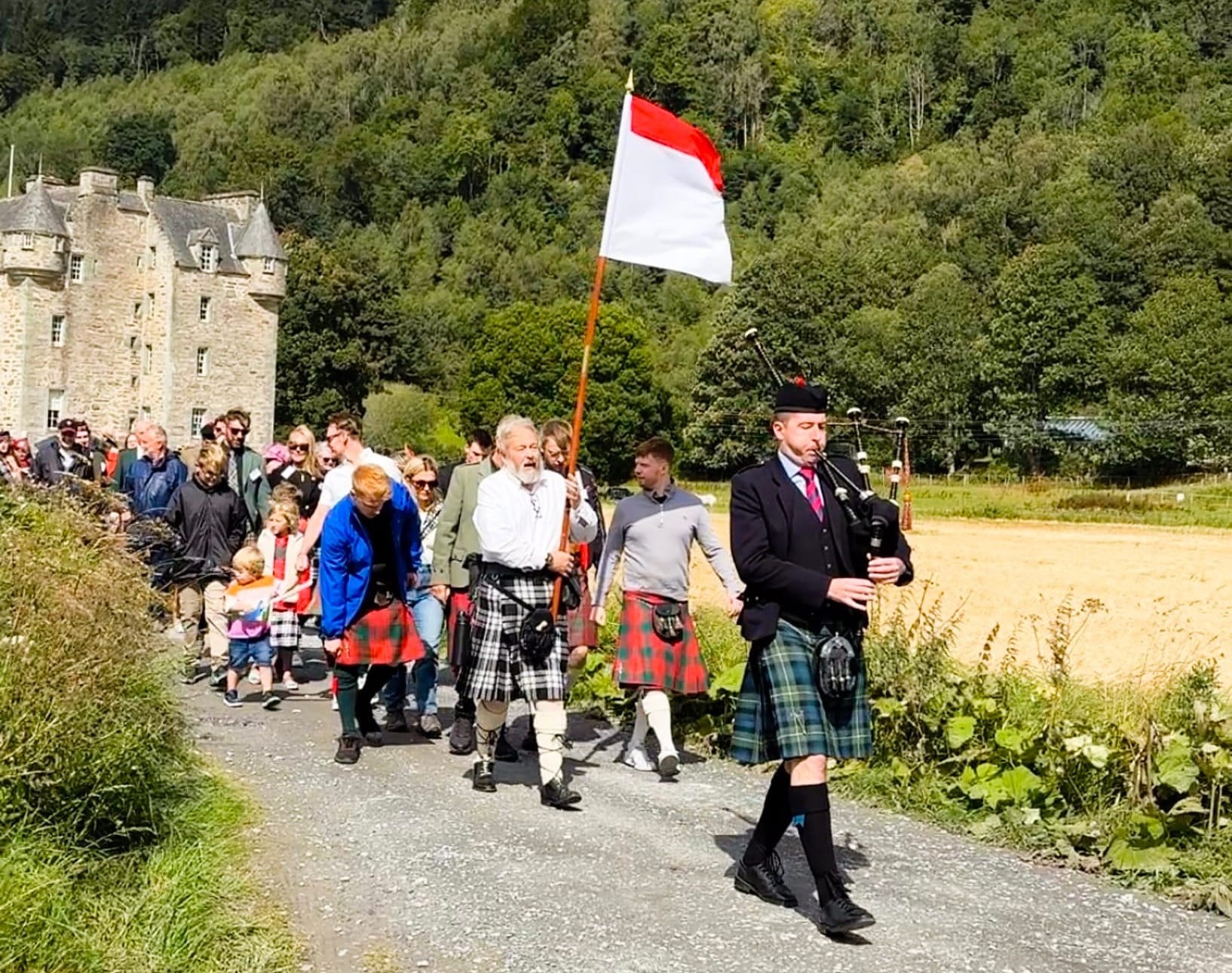 Led by a piper, people in kilts walk down the path from Castle Menzies.