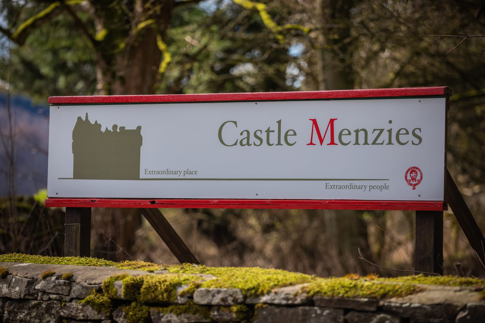 A sign for Castle Menzies next to a mossy stone wall.