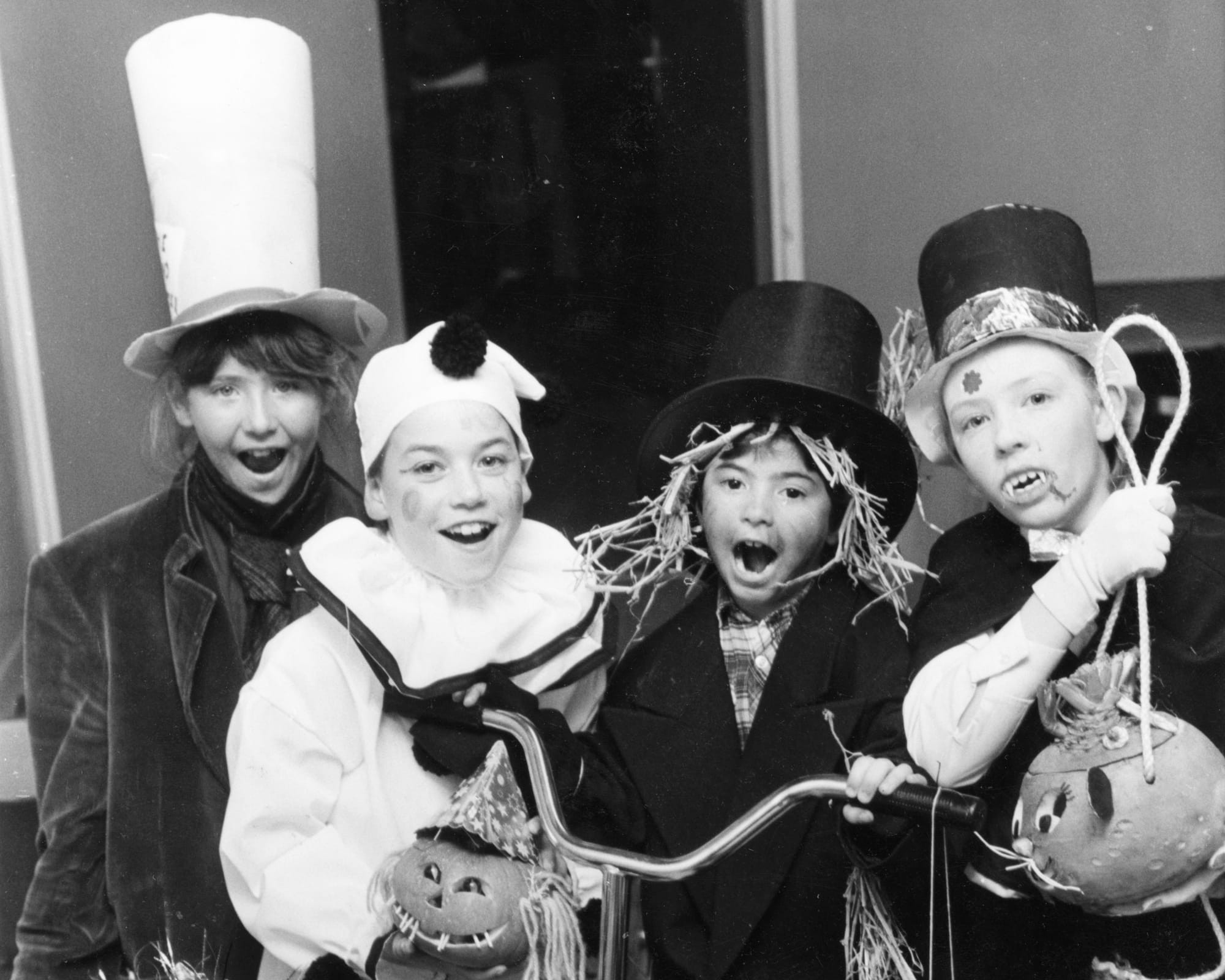 A black-and-white photo of children dressed up in costumes holding carved pumpkins.