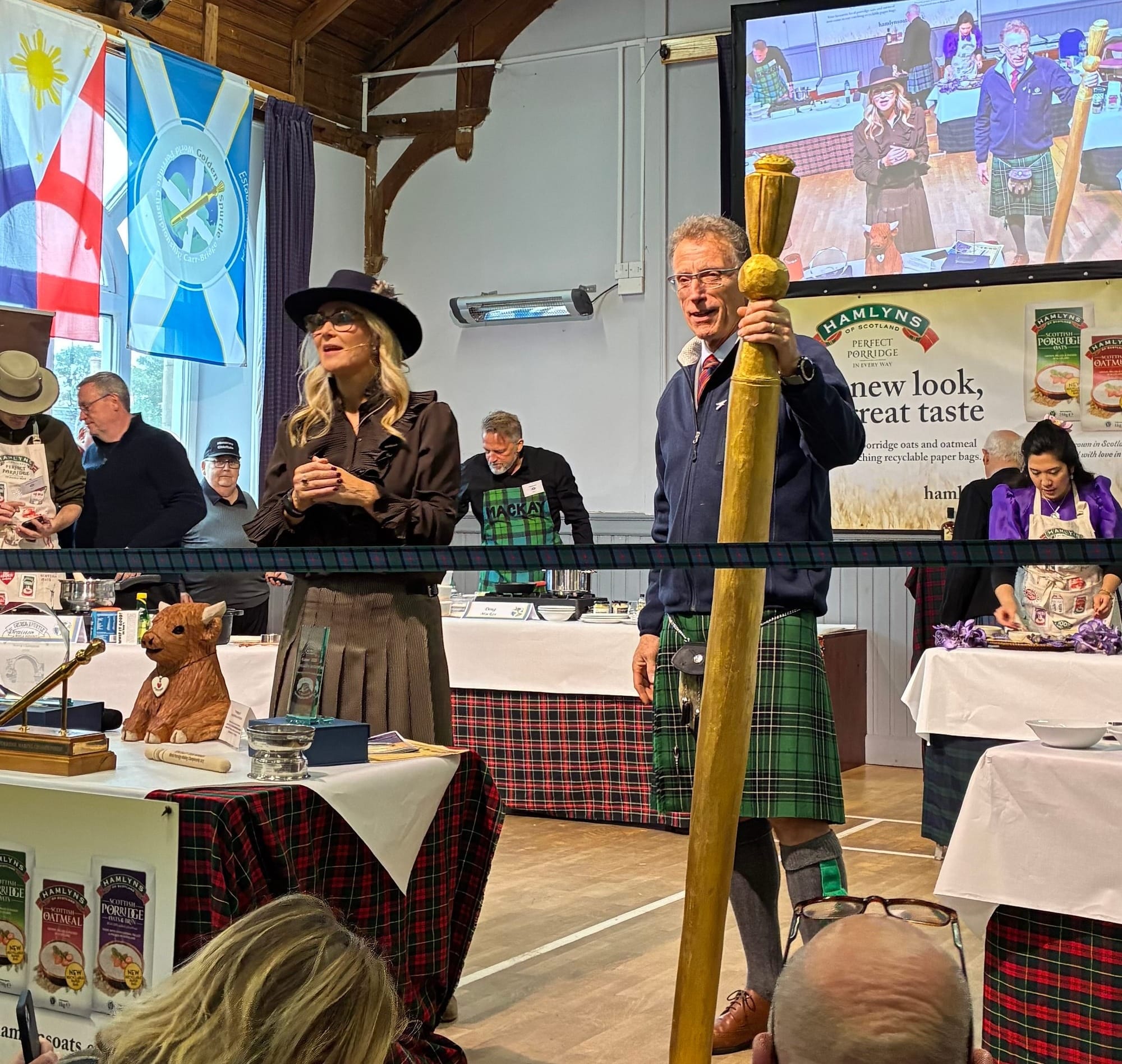 Host Sarah Rankin and porridge chieftain Alan Rankin open the event with a giant spurtle. Alan is wearing a kilt and holding a spurtle as large as him.