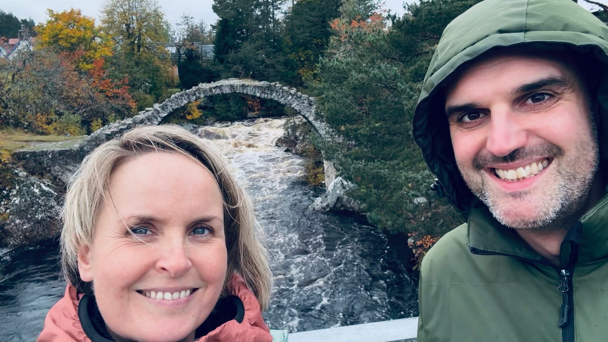 Rachel and her husband smile next to the coffin bridge in the rain.