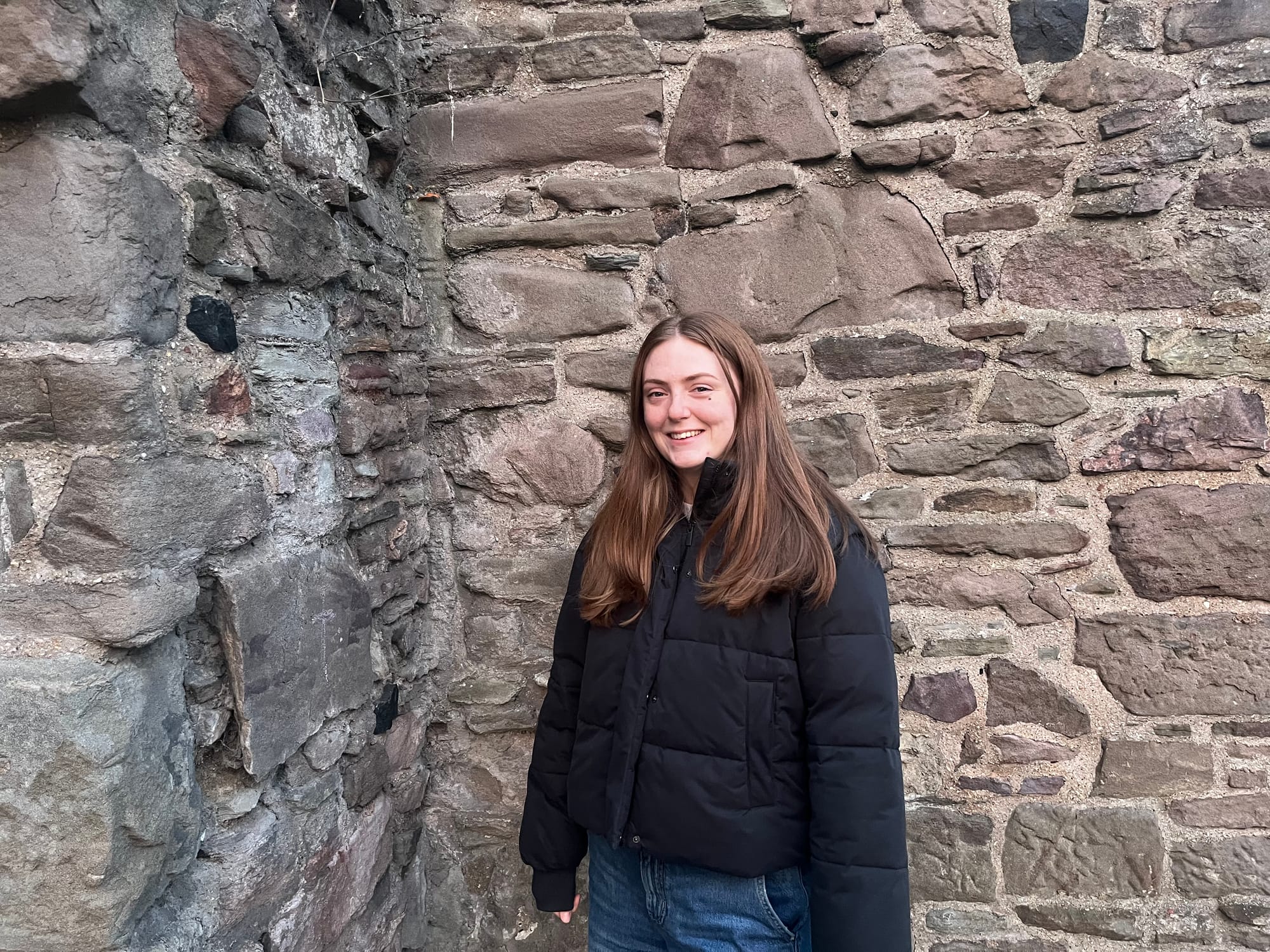 Beth smiles against an old stone wall.