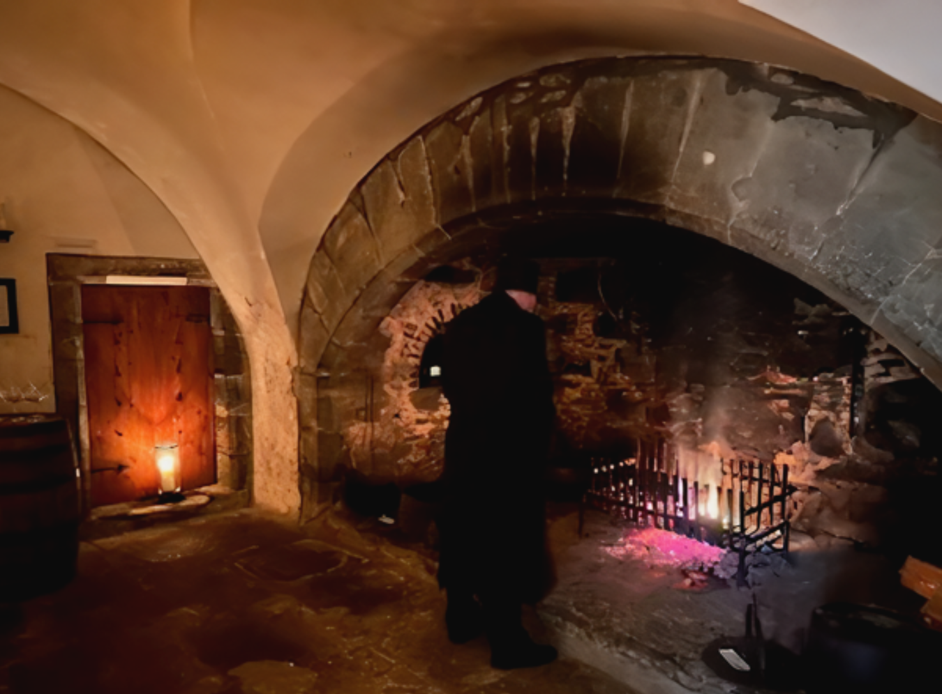 Gary, dressed all in black, looking at a fire in the castle's vaulted hearth in the kitchen.