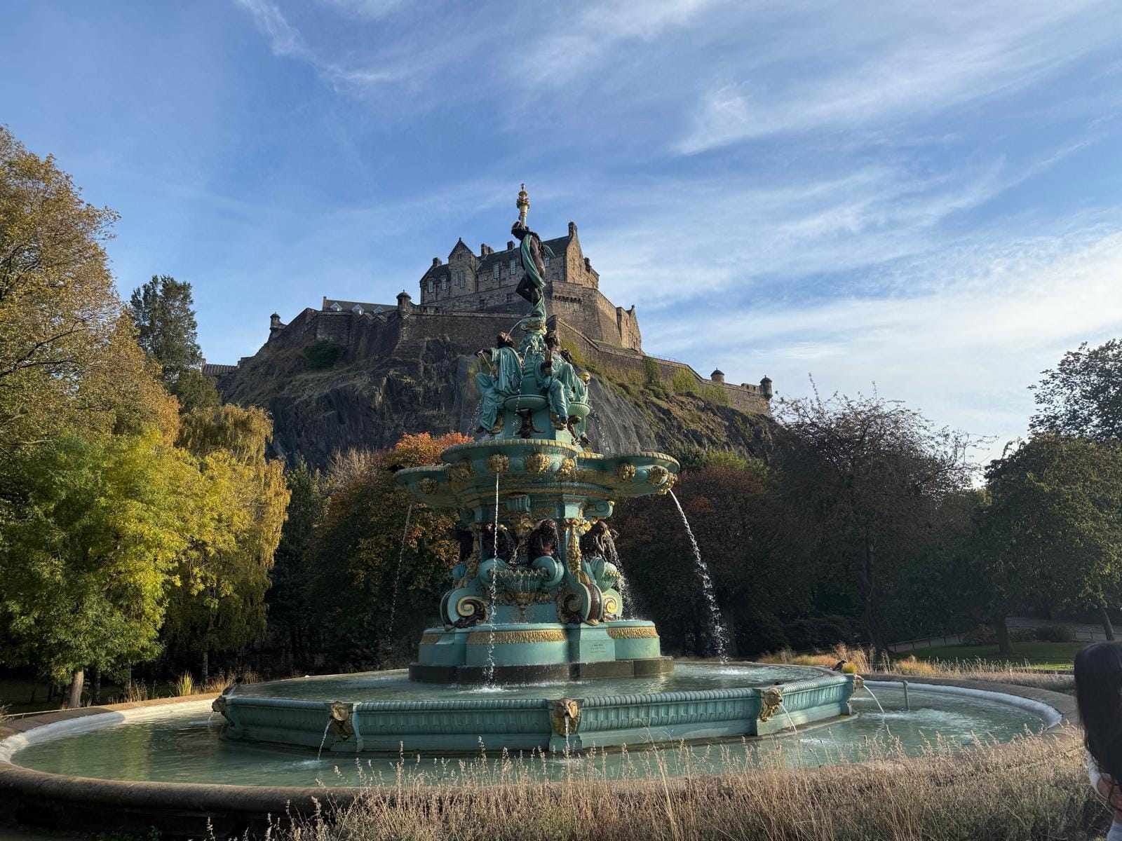 Ross Fountain is surrounded by large trees and a beautiful view of Edinburgh Castle