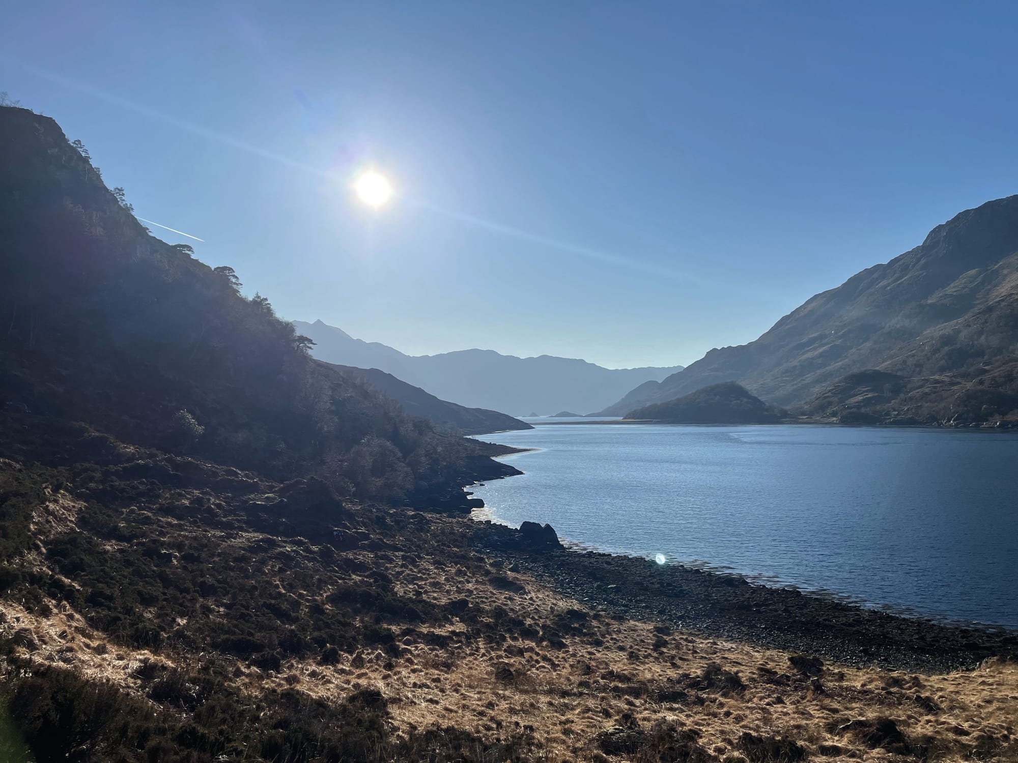 The sun high in the sky over Loch Hourn on the path along by the water.