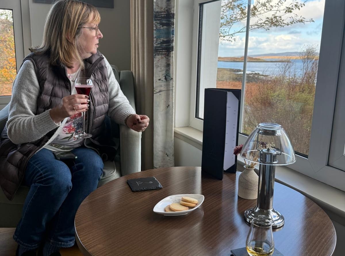 Anne, Daniella's mother in law, in the sitting room of The Three Chimneys enjoying a welcome drink. Daniella's dram of whisky sits on the table.