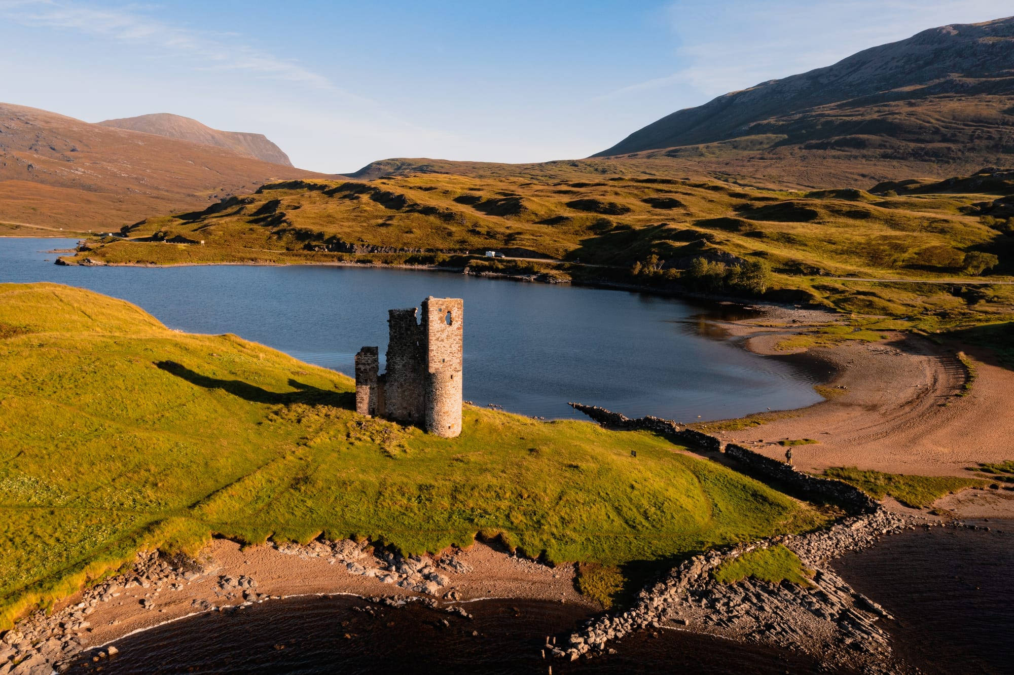 An aerial shot of Ardvreck Castle showing the varied landscape around it - grass, sandy beaches, rocks and a loch.