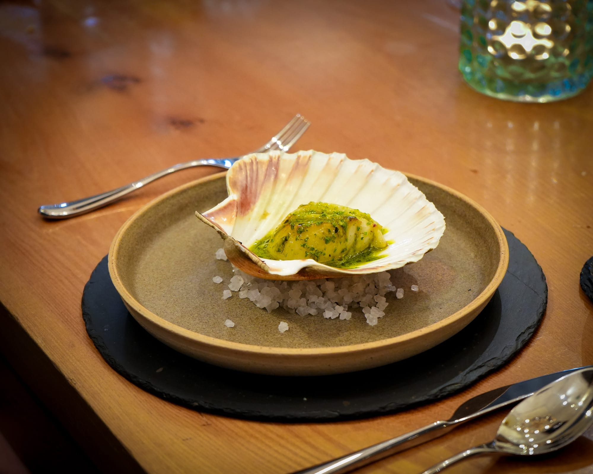 A cooked scallop covered in green sauce served in a scallop shell at The Three Chimneys