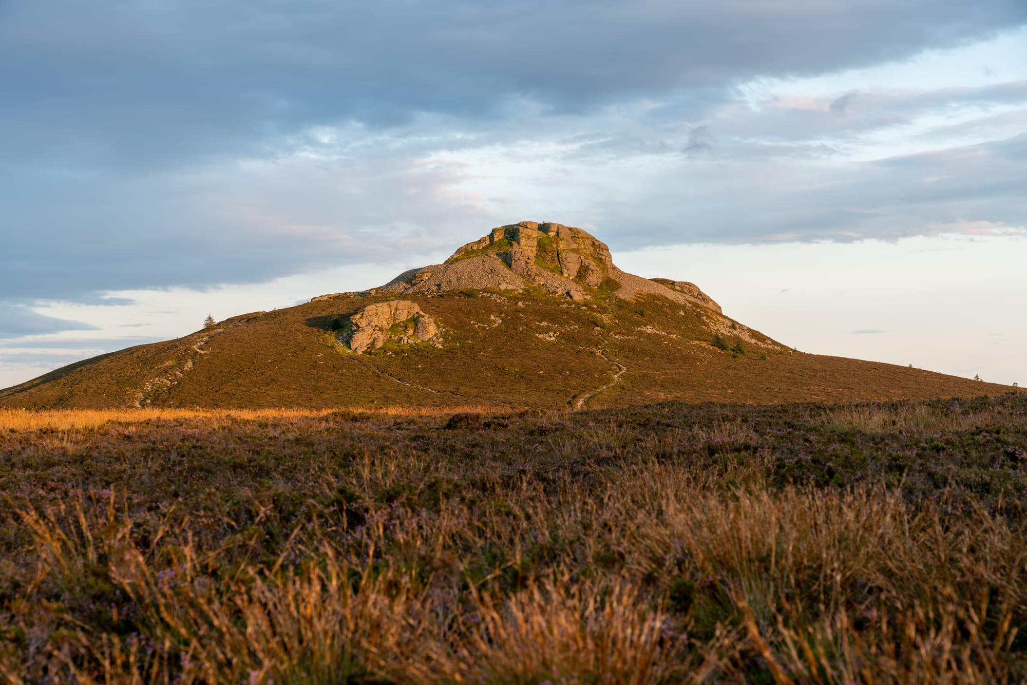 A high rocky hill with grass and heather leading up to its stony summit.