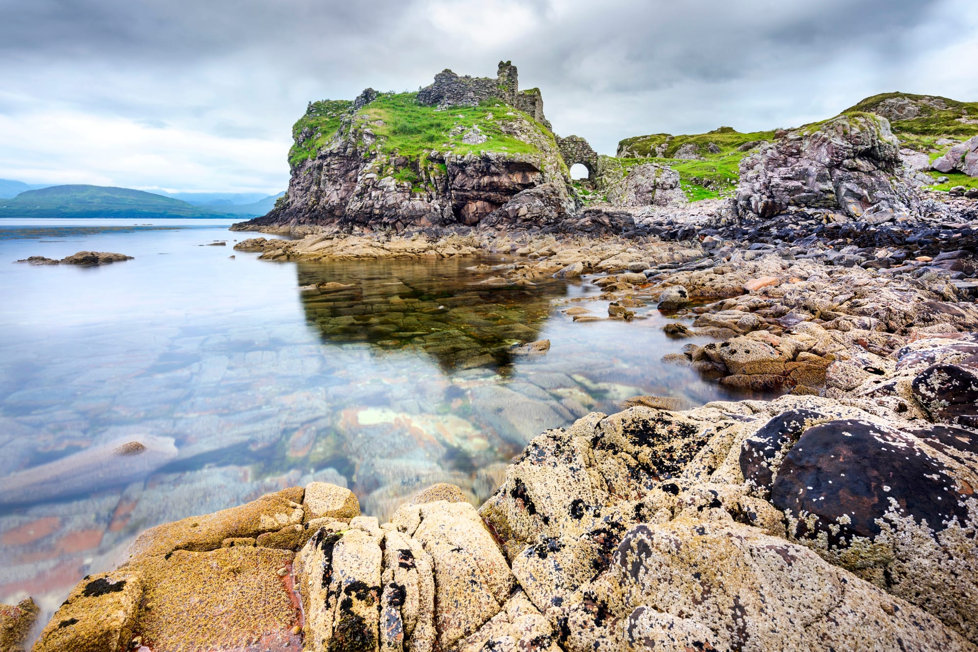 Ruins of a castle on a rocky outcrop jutting into calm waters.