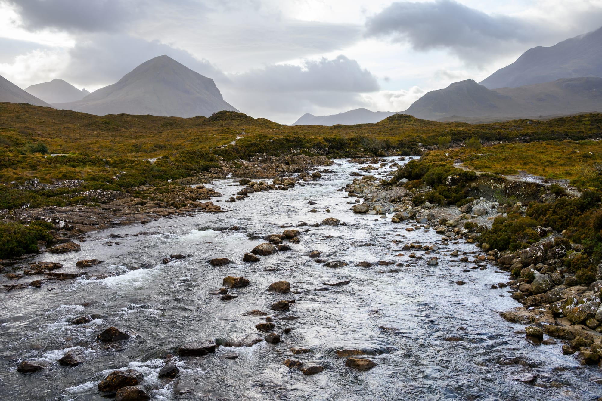 A shallow river tumbles over rocks and stone leading toward high mountains on Skye.