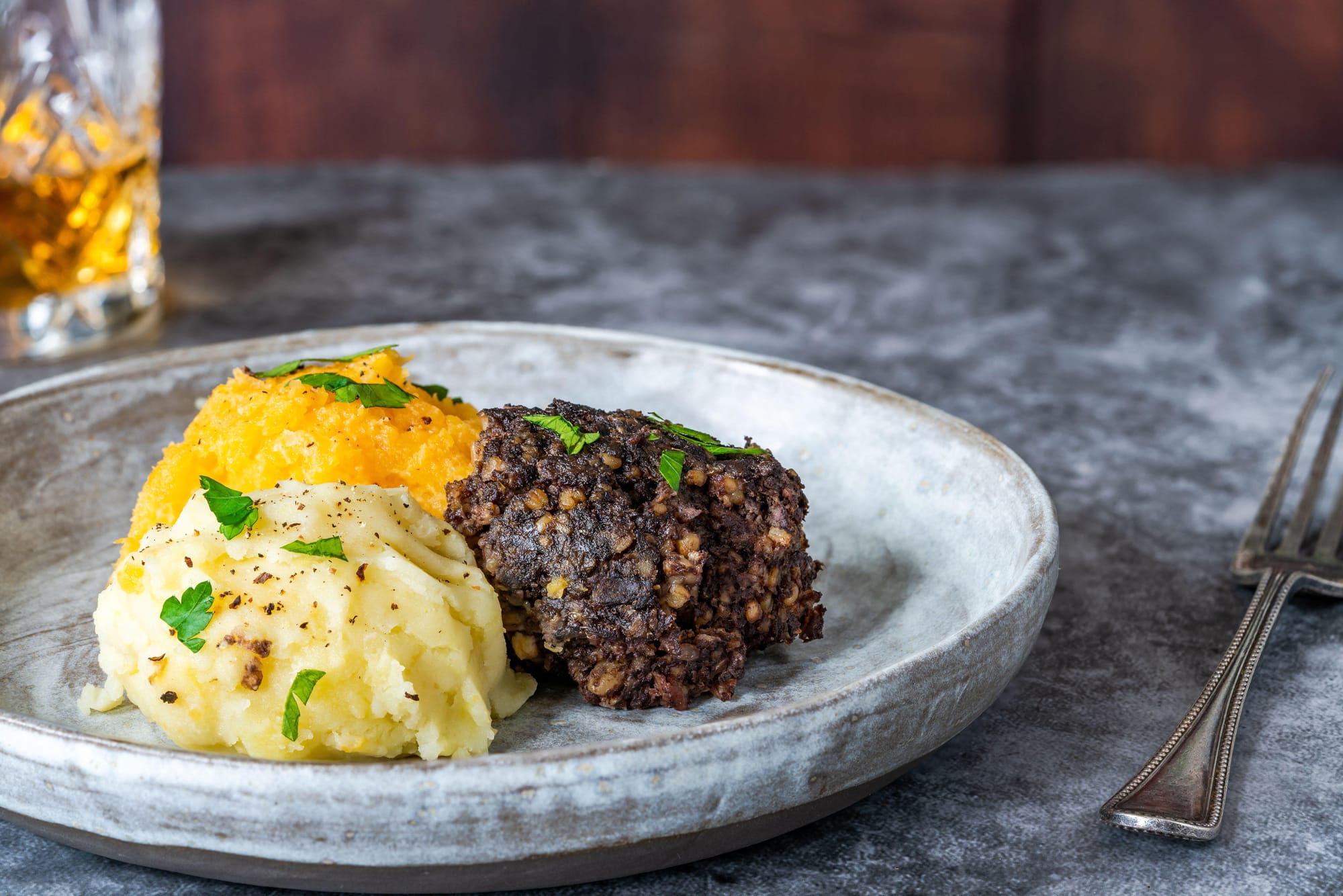 A round rustic plate of haggis, neeps and tatties topped with parsley.