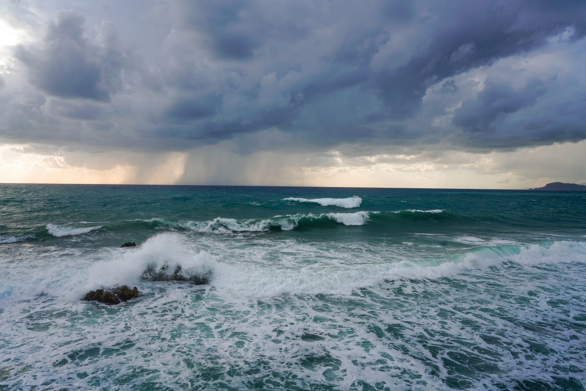 A stormy sea with dark clouds and rain on the horizon.