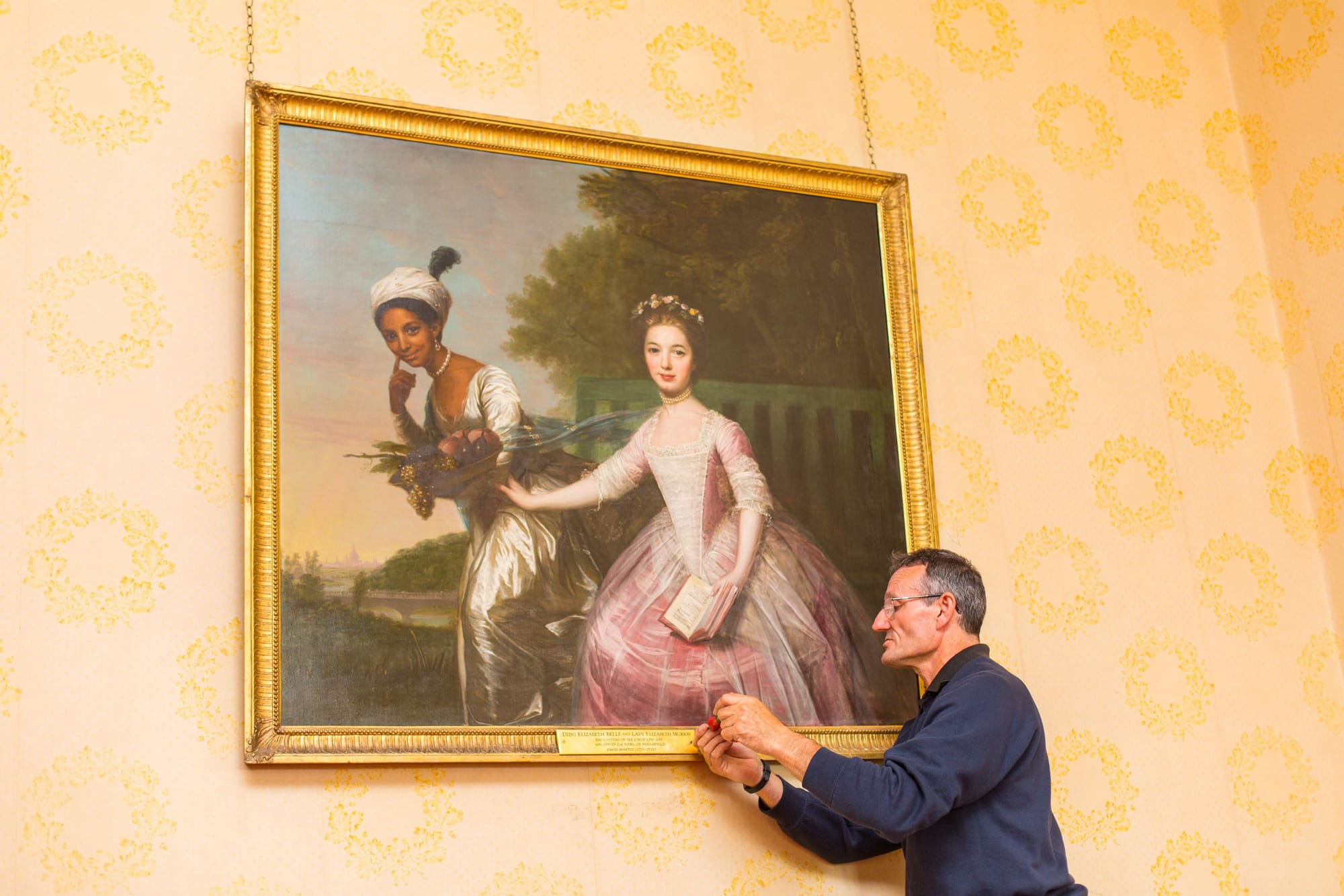 A painting of a young black woman in a silk dress with a white woman in pink dress hanging on a wall.
