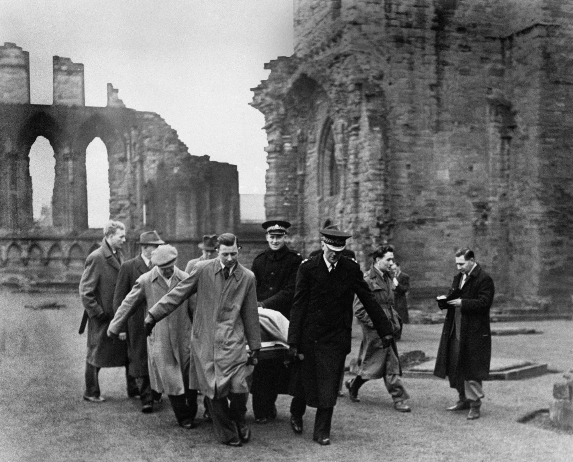 A black-and-white photo of men and police officers removing the stone from Arbroath Abbey.