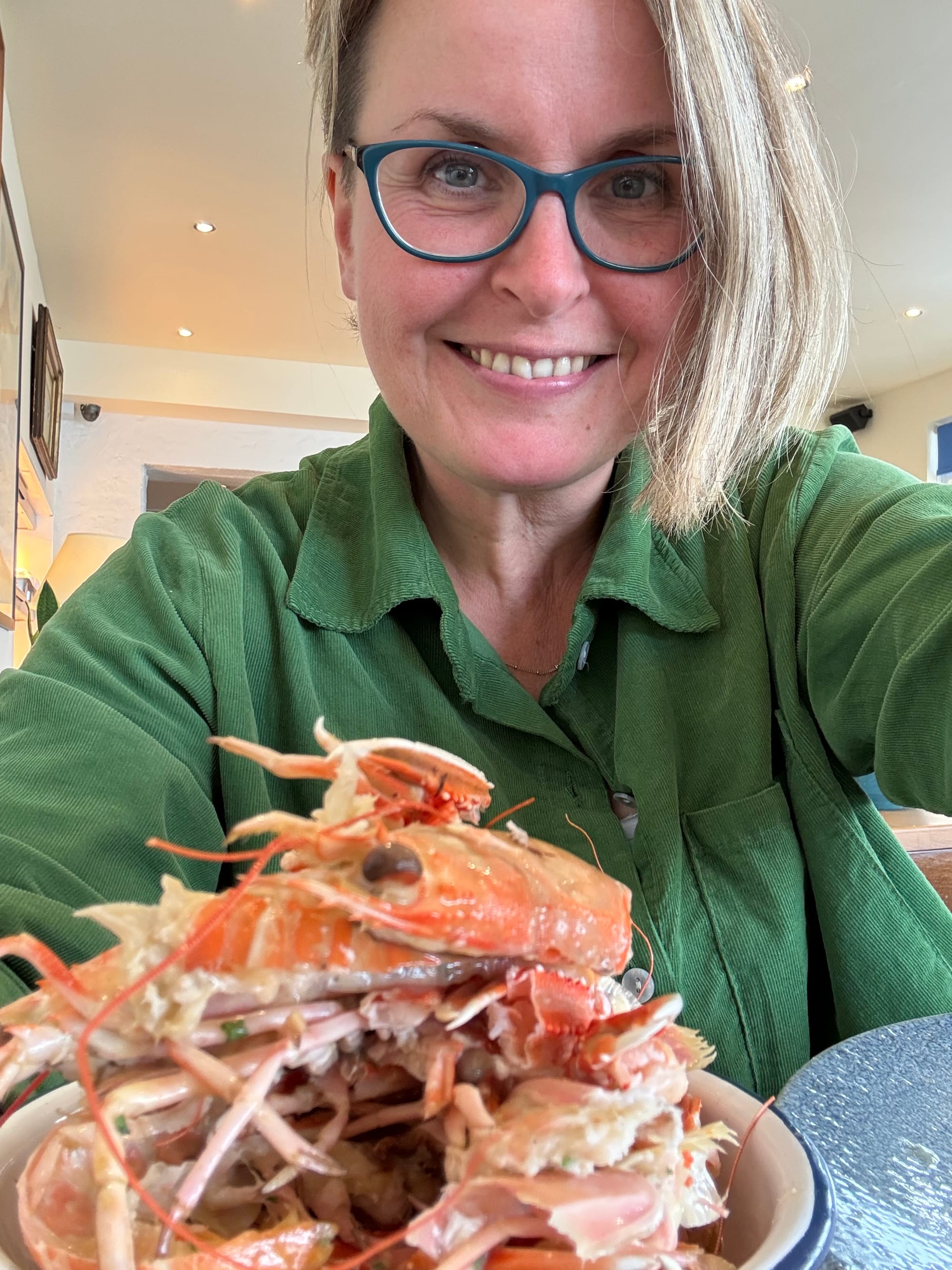 A woman with short blond hair in a green cord shirt smiled into the camera with a bowl of langoustine shells on the table.