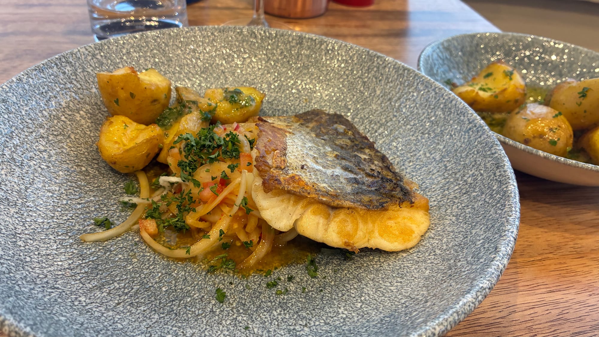 A fillet of hake crispy skin up on salsa with a pile of buttered potatoes next to it on a grey plate.