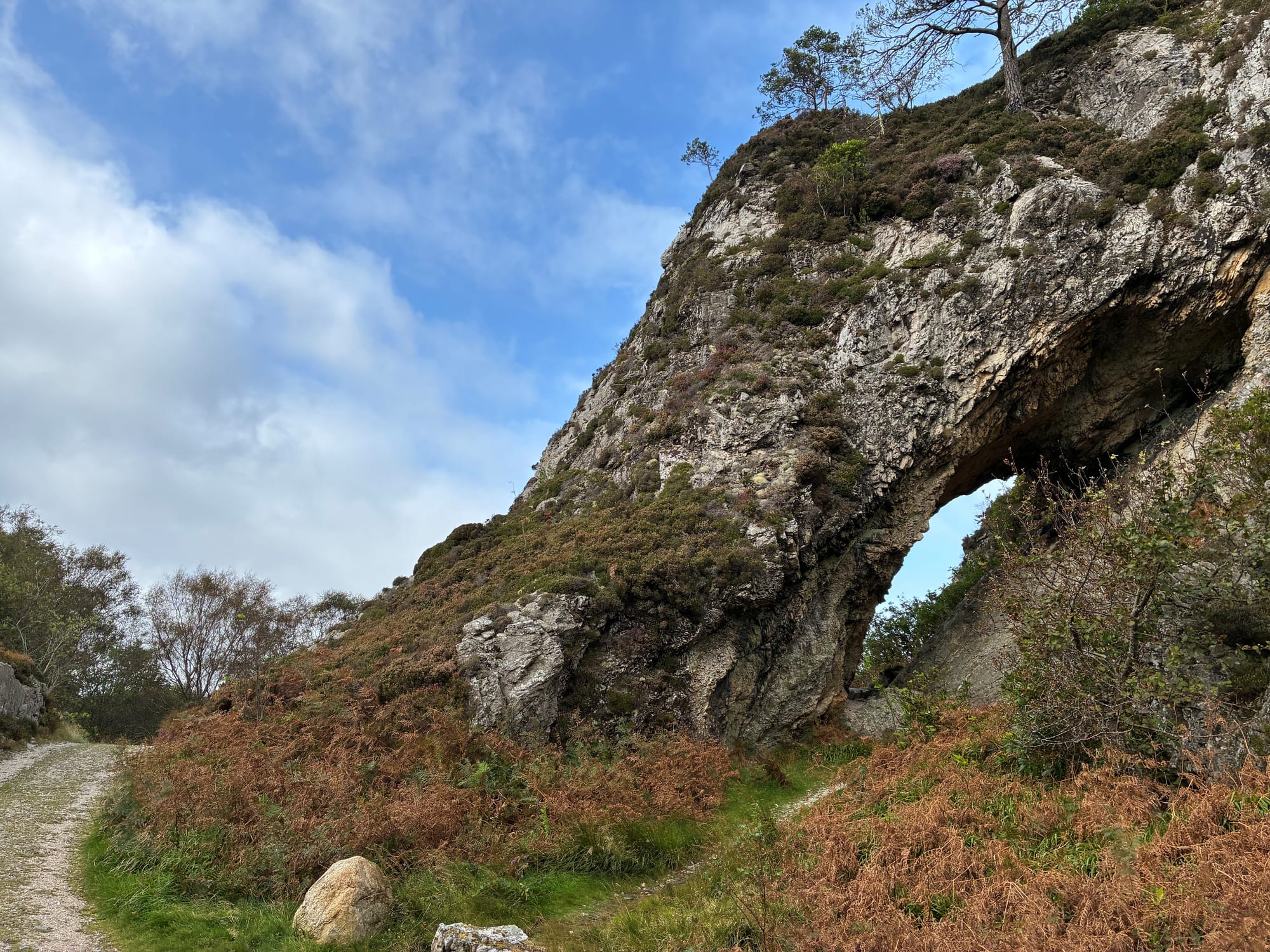 A sea arch in the cliff with a long oval shape next to a gravel path.