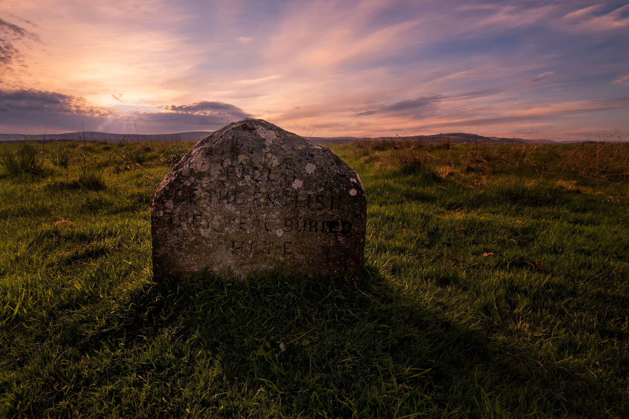 A memorial stone on the grassy battlefield, with the sun setting behind it.