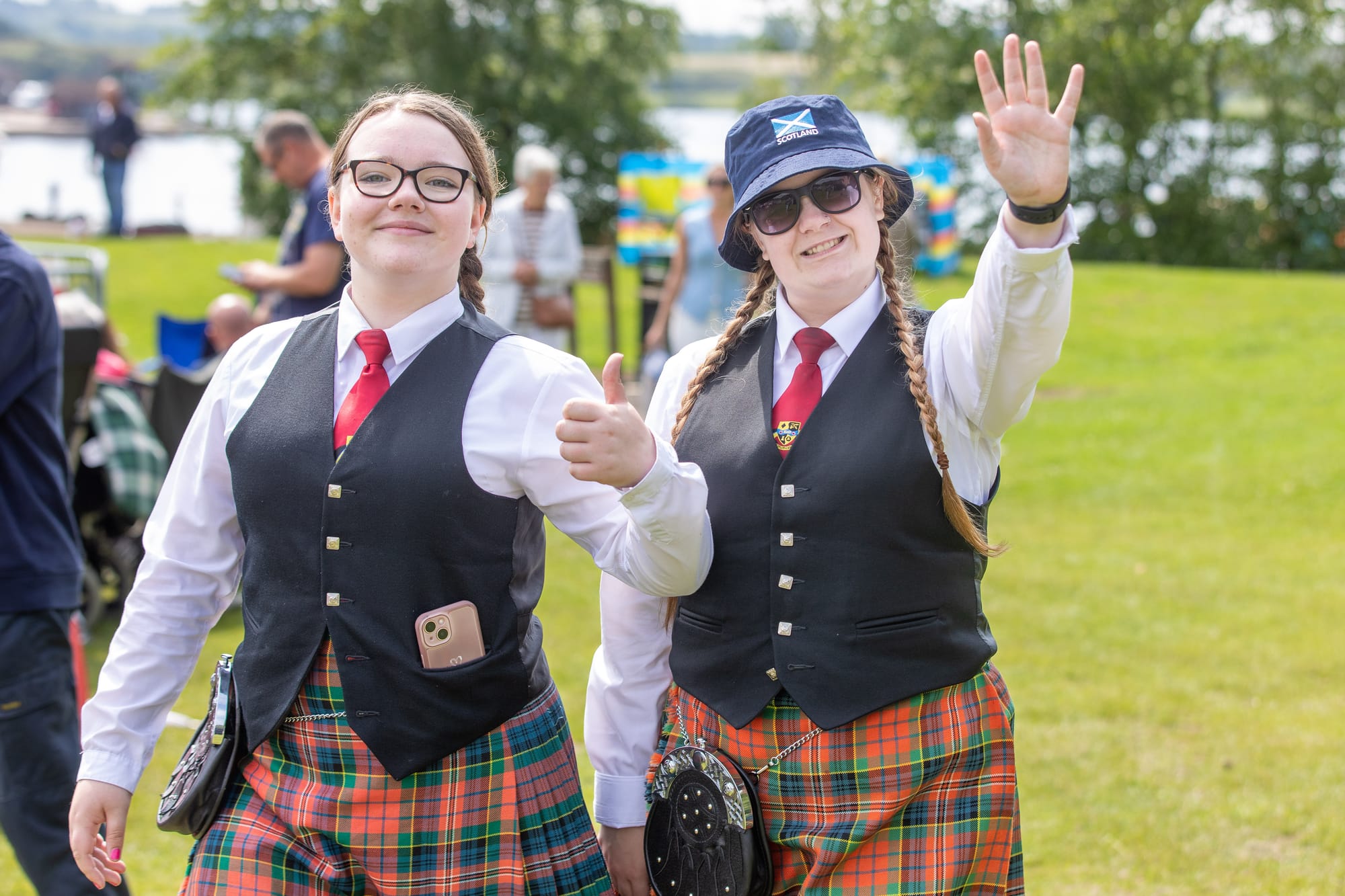 Two female pipe band members wave and smile at the camera.